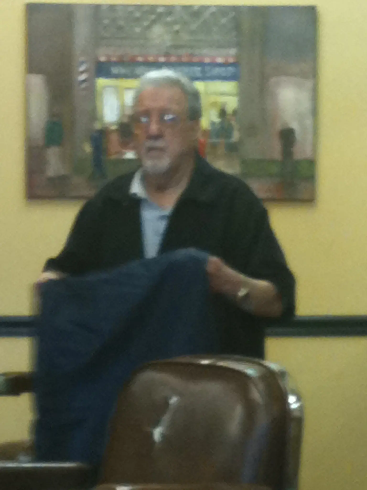 Barber relaxing in Wheaton Barber Shop with the storefront painting behind him